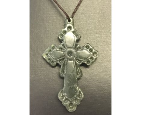 A carved green jade cross pendant on a thin cord thong.  