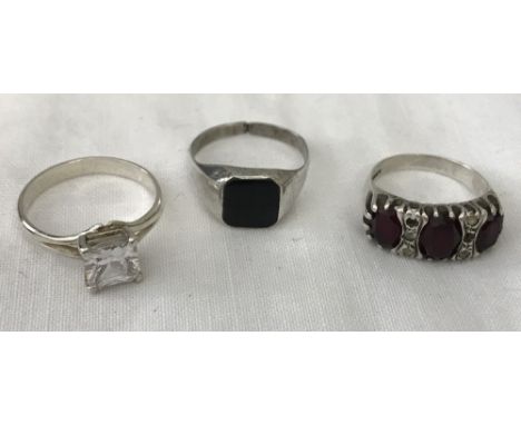 3 silver rings. A silver signet (a/f) a silver ring with central square cut clear stone and a silver garnet set trilogy ring 