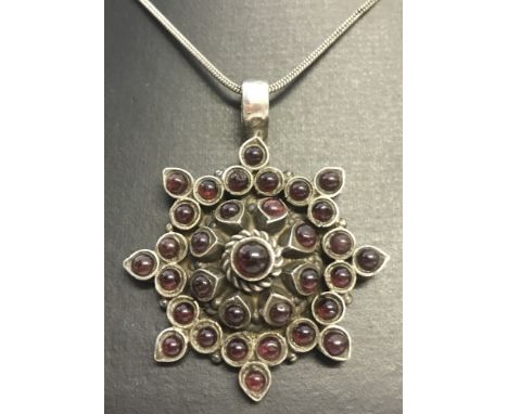 A large star shaped silver pendant sent with 33 round cut cabochon garnets. On a 18 inch silver snake chain. 