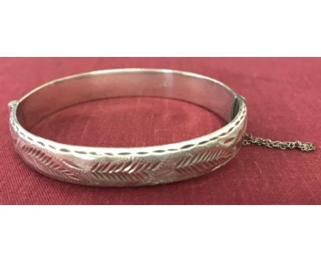 A Vintage silver bangle with half engraved detail and safety chain.  