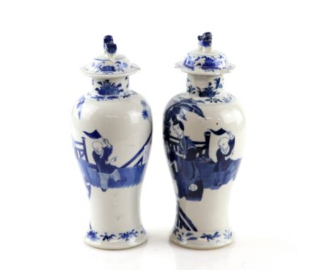 A pair of Chinese blue and white vases; each one with a domed cover and dog-of-fo finial, decorated with a group of Manchu/Ch