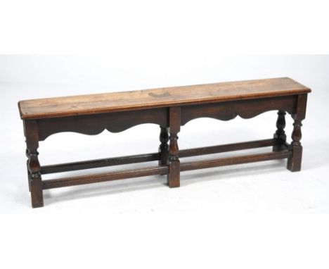 An 18th Century style oak stool
The rectangular plank top above a wavy frieze raised upon four turned baluster supports, legs