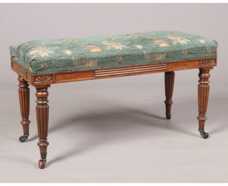 A Victorian carved mahogany duet stool. With overstuffed seat and raised on reeded tapering supports, 94cm x 40cm, 52cm high.