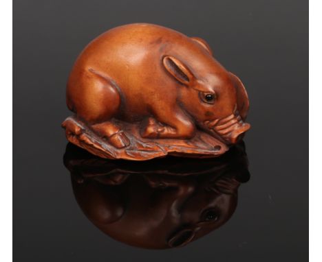 A 20th century Japanese carved fruitwood netsuke. Formed as a pig resting on a bed of leaves and having glass inset eyes, 4.7