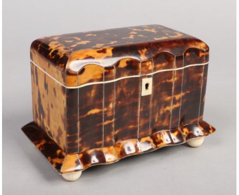 A 19th century tortoiseshell tea caddy with scalloped front. Housing two lidded compartments and raised on turned ivory ball 