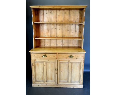 A Pine Dresser, the boarded shelf back above two drawers with brass cup handles above two panelled doors raised upon a plinth