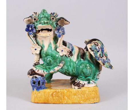 A CHINESE EARTHENWARE MODEL OF A DOG OF FOO / LION DOG,  painted in blue,green,brown and yellows, stood with its paw upon a p