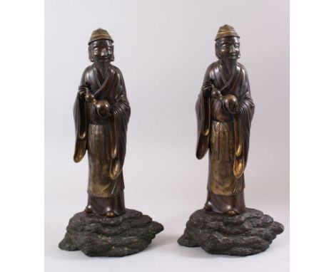 A PAIR OF JAPANESE MEIJI PERIOD BRONZE OKIMONO OF A SCHOLAR OR SAGE, stood upon a rocky outcrop simulated base, wearing tradi