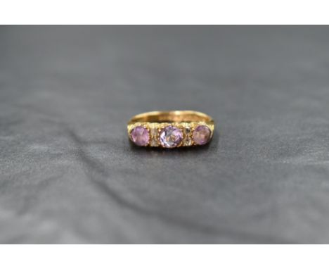 An 18ct gold three stone amethyst ring interspersed by 2 pairs of diamond chips, all in an indented gallery mount with moulde