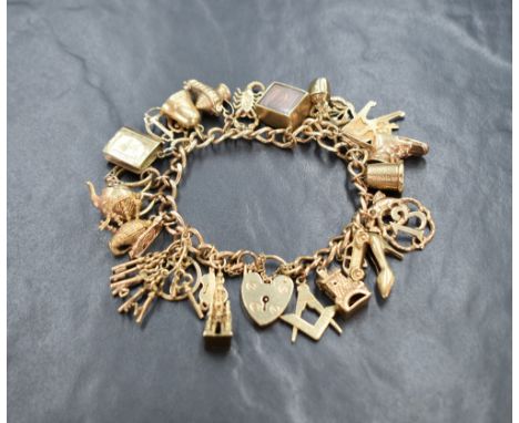 A 9ct gold charm bracelet having padlock clasp and 26 charms including bagpipes, £10 emergency box, shoes, keys etc, approx 5