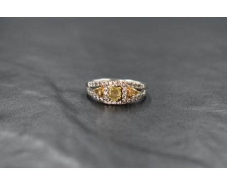 An 18ct white gold diamond ring, the central cushion cut yellow diamond measuring approximately 0.37ct within a white diamond