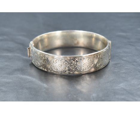 A 1960's silver hinged bangle, having decorative scroll engraving to one side and an extending opening, approximately 6.5cm d