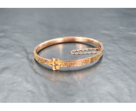 A early 20th Century 9ct rose gold hinged bangle modelled as a belt with scroll decoration, hallmarks for Chester 1911, inner