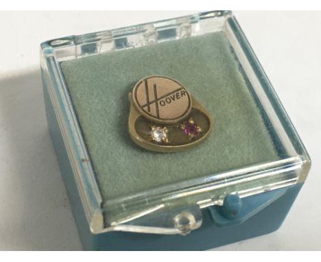 A miniature gold Hoover pin set with a small diamond and ruby. Postage category A