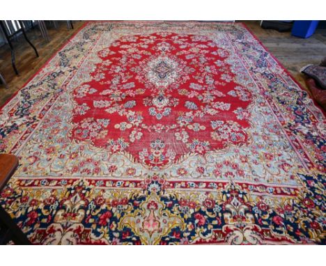 A large Persian Kerman red ground carpet with traditional floral design around the central medallion, within conforming navy 