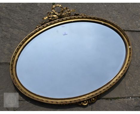 An Edwardian Sheraton Revival oval gilt framed mirror, with bevelled plate, surmounted by a ribbon bow, 85 cm h x 98 cm w