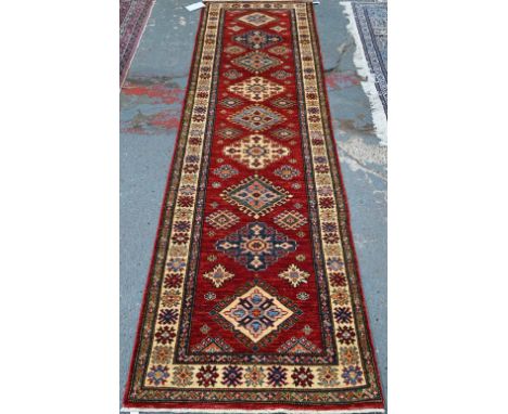 A Persian Kazhak runner with geometric medallions on red ground with blue and beige borders, 282 x 80 cm
