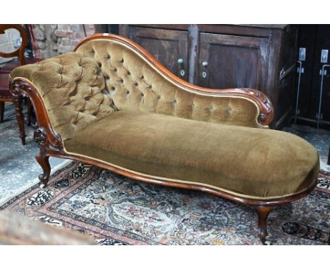 A Victorian carved and moulded mahogany framed chaise longue, the green velvet buttoned scroll back over a serpentine form se