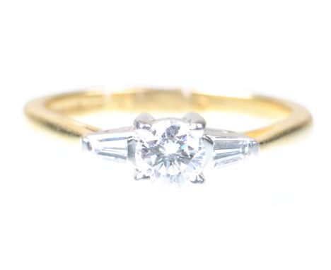 A diamond three stone ring 
The round brilliant-cut diamond flanked by tapered baguette-cut diamonds, to an 18ct gold shank, 