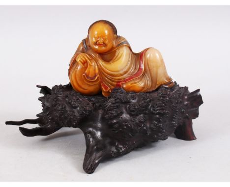 A GOOD QUALITY CHINESE CARVED SOAPSTONE FIGURE OF LUOHAN ON NATURALISTIC BASE, the luohan in a leaning position, with signs o