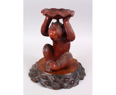 A JAPANESE MEIJI PERIOD CARVED HARDWOOD STAND IN THE FORM OF A MONKEY, the monkey realistically carved holding a lily pad abo