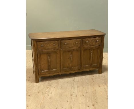 An Ercol oak sideboard with shaped rectangular top above three drawers and three inset panel doors (h.86cm x l.145cm x d.52cm
