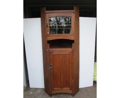 A Liberty &amp; Co Arts &amp; Crafts oak corner cabinet of architectural form, leaded glazed top section over open shelf and 