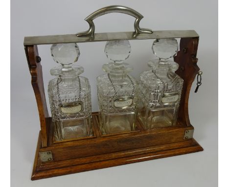 Edwardian three bottle Tantalus with cut glass decanters. Retailed by Rowe Jewellery, Marlow. With hallmarked silver Whisky, 