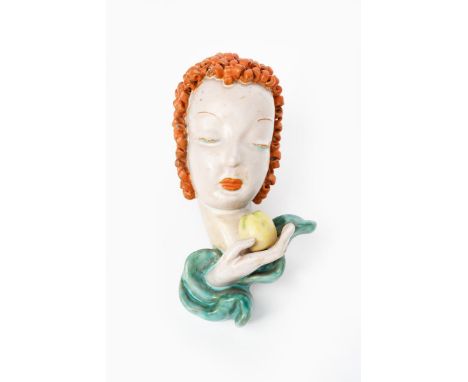 A Goldscheider Pottery wall mask, model no.6774, modelled as a woman with orange curly hair, holding an apple, glazed in colo