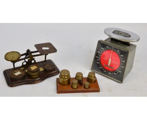 A set of brass postal scales with associated weights on a shaped wooden plinth and a set of bell postal weights on a wooden s