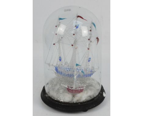 A blown glass model of a three masted ship with further smaller ships beside and lighthouse, mounted underneath a glass dome,