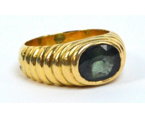 An 18ct green sapphire ring, the large oval collet set stone mounted in ribbed shoulders, size P, approx 13.7g.