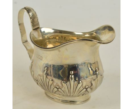 A Victorian hallmarked silver cream jug with embossed decoration to the lower part of the body and with loop handle, on taper