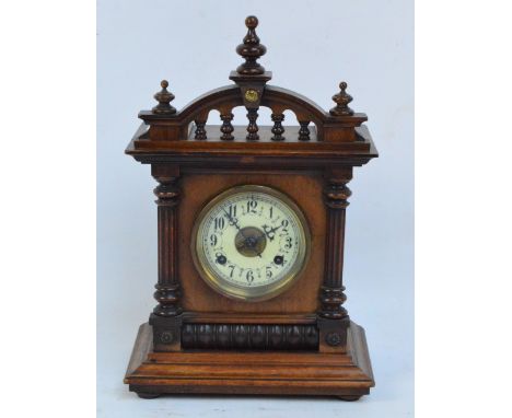 A c.1900 walnut and stained beech mantel clock with circular dial set with Arabic numerals beneath a raised pediment, height 