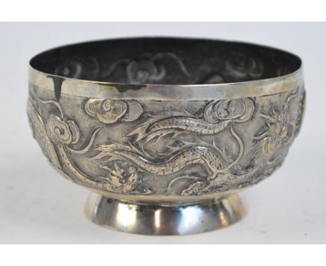 A c.1900 Chinese white metal dragon bowl, overall embossed with dragons chasing the pearl of wisdom amongst clouds, raised on