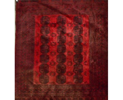 An Afghan Bokhara designed carpet with central red ground panel set with three rows of elephant foot medallions within a mult
