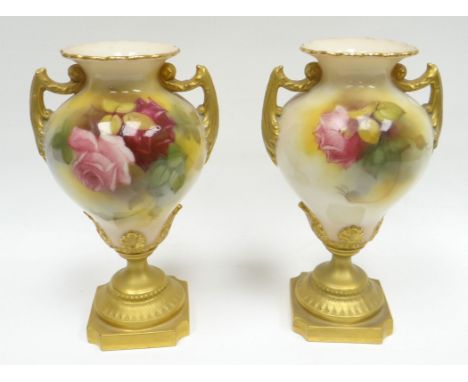 A pair of Royal Worcester pedestal vases, the blush bodies painted with pink and red roses amongst leaves, with twin gilt han