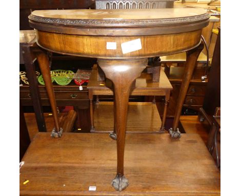 An early 20th century walnut and figured walnut demi lune fold over baize lined card table, having acanthus leaf carved edge 