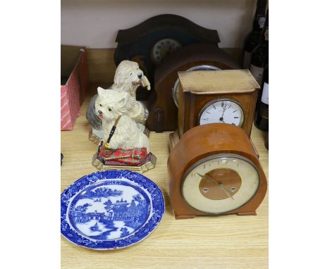 A tin mantel clock and 3 wooden clocks, 2 dog door stops and a blue and white plate.