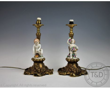 A pair of 20th century figural candlesticks, each gilt brass candlestick on a rococo base mounted with a model of a Cherub ha
