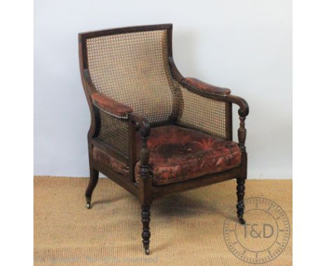 A George IV carved mahogany library chair, with a curved back inset with curved caning, with caned sides and seat, the arms w