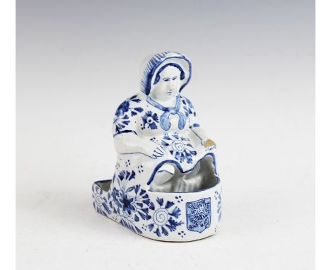 A Delft stand in the form of a seated woman, 19th century, probably a pipe rack, the amusing figure modelled wearing a bonnet