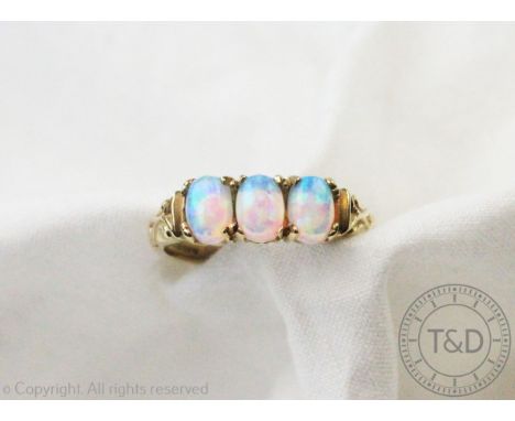 A three stone opal ring, the three oval, untested opals all set in 9ct yellow gold, to the scroll carved shoulders and plain 