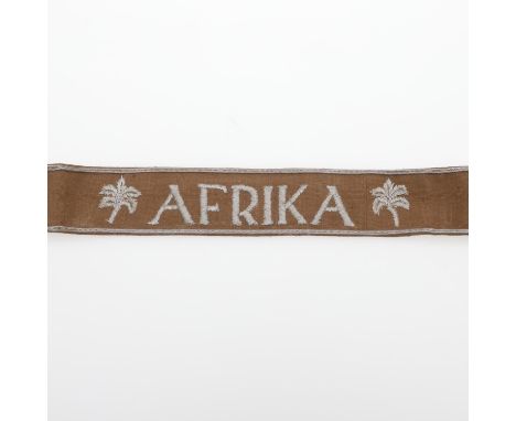 A machine embroidered cuff title for the Afrika Corps, 'AFRIKA' between palm trees and borders, against a light brown cotton 