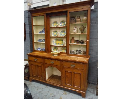 A late 19th Century light oak dresser with inverted glazed cupboard rack over a base fitted with three drawers centred by a r