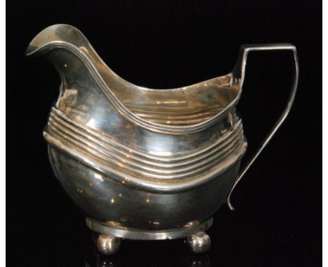 A George III hallmarked silver cream jug of cushion form with reeded border, scroll handle on four bun feet, London 1813 Thom