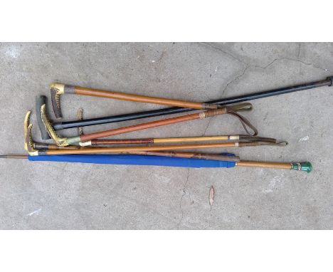 Five vintage riding crops with antler handles, an ebonised walking stick with silver collar, and an umbrella with glass handl