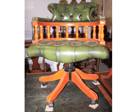 A polished as yew wood swivel desk chair, button upholstered in a green leather, on quadruple splay supports