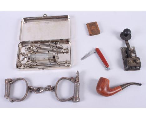 A pair of vintage handcuffs, stamped "Thiatt", a syringe set, a Bendix flame proof Morse key, a pipe, a vesta case and a pipe