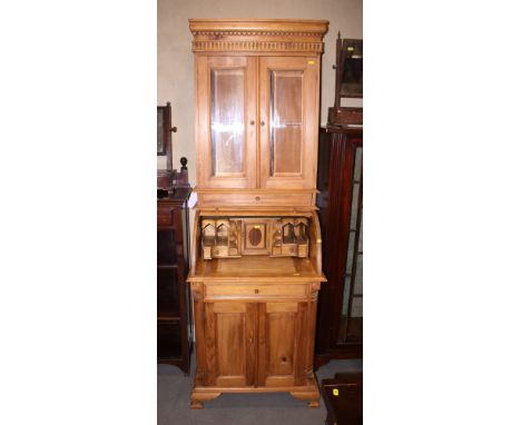 A stripped pine roll top bureau bookcase, the upper section enclosed glazed doors over fitted writing compartment and cupboar